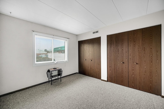 unfurnished bedroom with carpet, visible vents, baseboards, and two closets