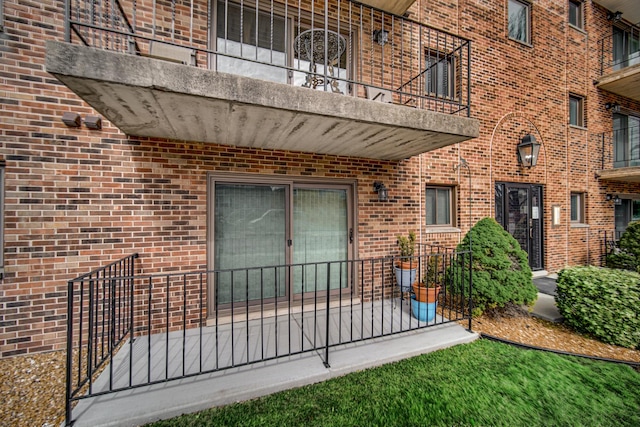 view of exterior entry featuring brick siding and a balcony