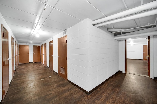 hallway with concrete block wall, visible vents, and wood finished floors