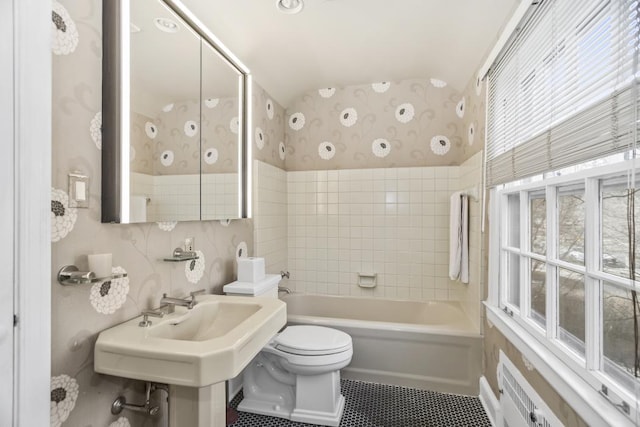 bathroom with tile walls, wallpapered walls, toilet,  shower combination, and tile patterned floors