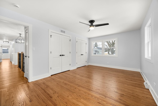 unfurnished bedroom with wood-type flooring, ceiling fan with notable chandelier, multiple windows, and two closets