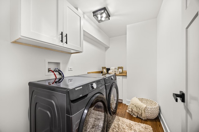 clothes washing area featuring dark wood-type flooring, washer and clothes dryer, and cabinets