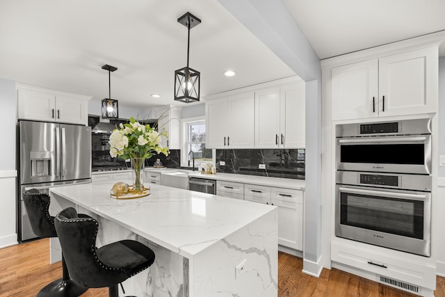 kitchen featuring pendant lighting, white cabinets, a center island, light stone counters, and stainless steel appliances