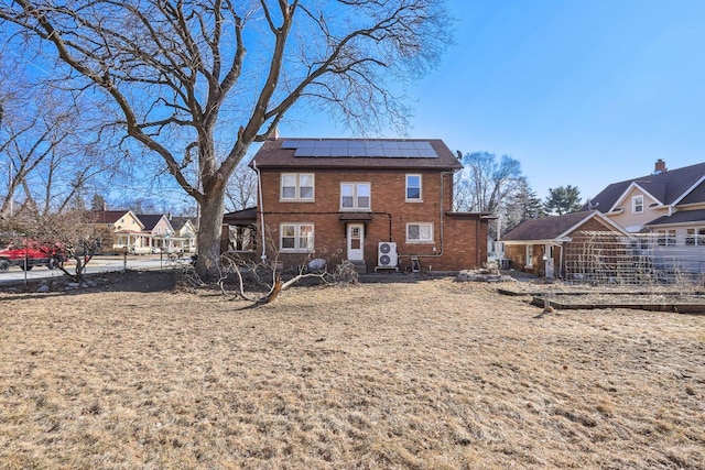 rear view of house featuring fence, solar panels, and brick siding