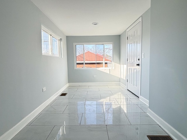 unfurnished room with a healthy amount of sunlight, marble finish floor, visible vents, and baseboards