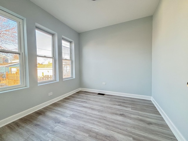 spare room with light wood-type flooring, visible vents, and baseboards