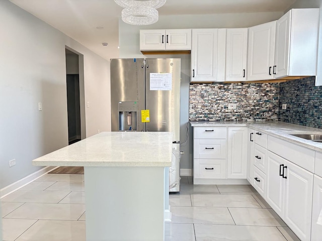 kitchen with light stone counters, white cabinets, stainless steel fridge with ice dispenser, and tasteful backsplash