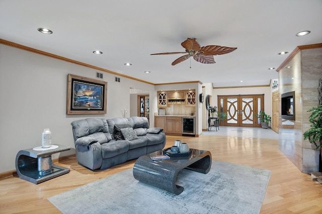 living room featuring crown molding, bar area, light wood-type flooring, ceiling fan, and beverage cooler