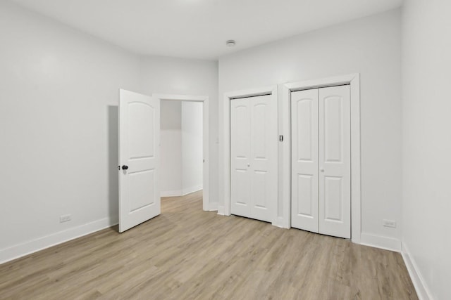 unfurnished bedroom featuring light hardwood / wood-style flooring and two closets