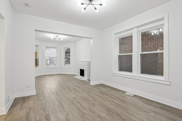 unfurnished living room featuring a tiled fireplace, wood-type flooring, and a notable chandelier