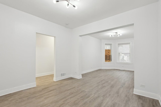 unfurnished room featuring a notable chandelier and light wood-type flooring