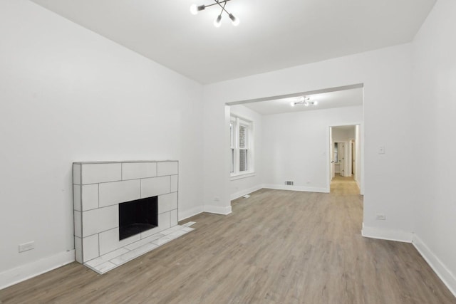 unfurnished living room with an inviting chandelier, a tiled fireplace, and light hardwood / wood-style flooring