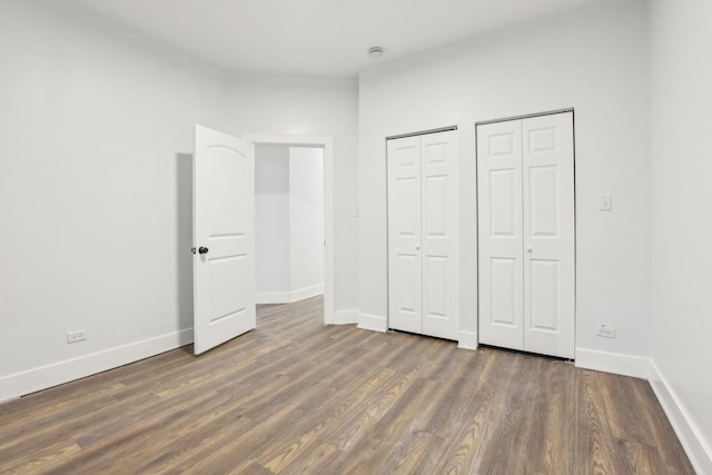 unfurnished bedroom featuring multiple closets and dark hardwood / wood-style floors