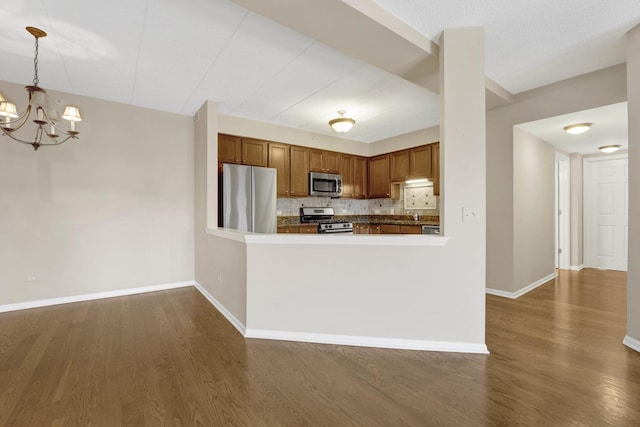 kitchen with tasteful backsplash, appliances with stainless steel finishes, pendant lighting, and dark hardwood / wood-style flooring