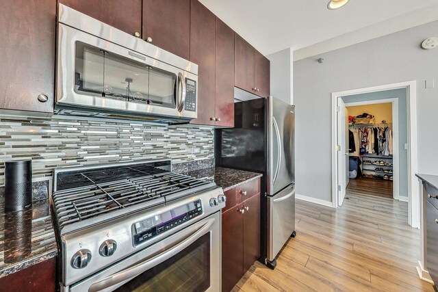 kitchen featuring appliances with stainless steel finishes, dark stone counters, light hardwood / wood-style flooring, and backsplash