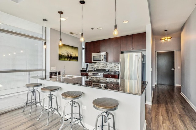 kitchen with dark brown cabinetry, sink, tasteful backsplash, dark stone counters, and stainless steel appliances