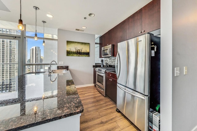 kitchen featuring sink, light hardwood / wood-style flooring, hanging light fixtures, appliances with stainless steel finishes, and dark stone counters