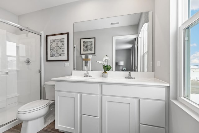 full bathroom featuring double vanity, a stall shower, toilet, wood finished floors, and a sink