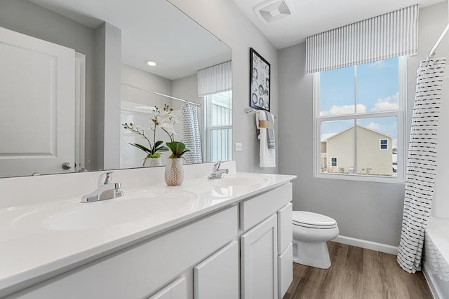 bathroom featuring toilet, wood finished floors, a sink, visible vents, and double vanity