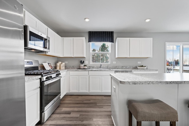 kitchen with stainless steel appliances, a sink, a kitchen breakfast bar, light countertops, and dark wood-style floors