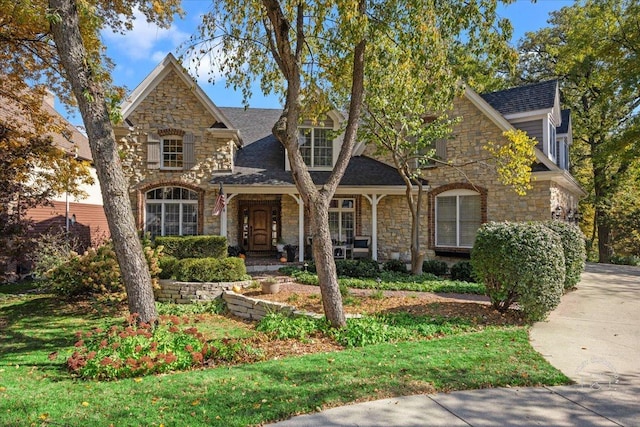 view of front of property with stone siding, a porch, and roof with shingles