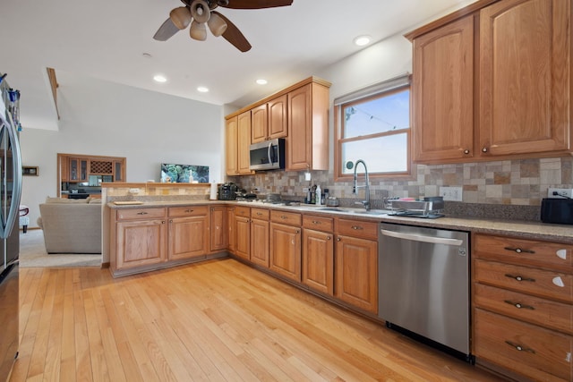 kitchen featuring light wood finished floors, a peninsula, a sink, decorative backsplash, and appliances with stainless steel finishes