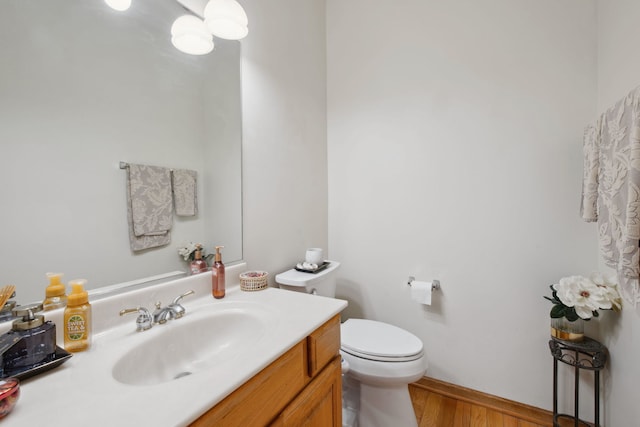 half bathroom featuring toilet, wood finished floors, and vanity