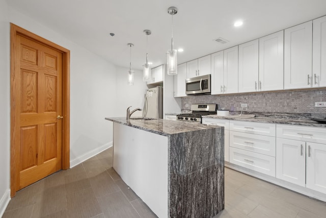 kitchen featuring a kitchen island with sink, a sink, stainless steel appliances, stone counters, and decorative backsplash