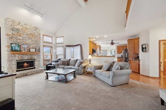 living area featuring high vaulted ceiling, light wood-style flooring, a ceiling fan, a stone fireplace, and rail lighting