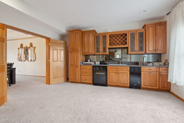 kitchen with brown cabinetry, beverage cooler, light colored carpet, and a sink