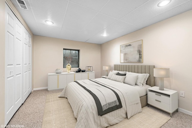 bedroom featuring baseboards, visible vents, a drop ceiling, and light carpet