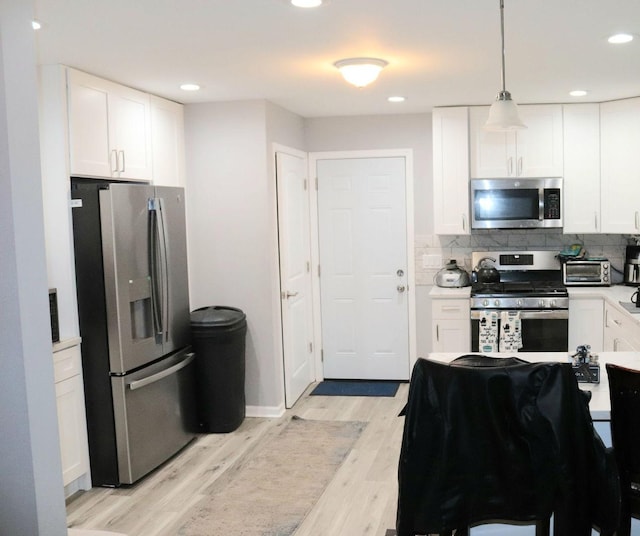 kitchen featuring stainless steel appliances, tasteful backsplash, white cabinets, decorative light fixtures, and light wood-type flooring