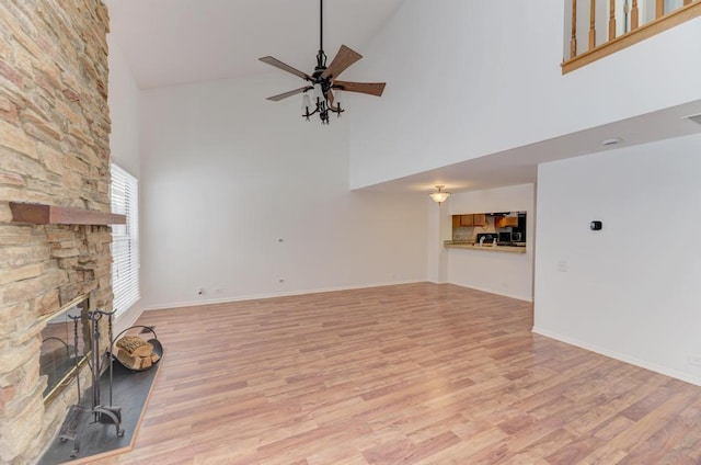 unfurnished living room with a fireplace, ceiling fan, light hardwood / wood-style floors, and a high ceiling