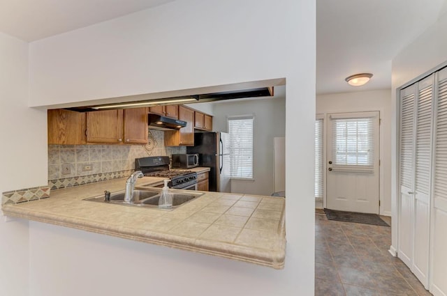 kitchen with tile countertops, kitchen peninsula, stainless steel appliances, sink, and decorative backsplash