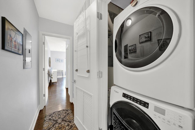 washroom featuring dark wood-style flooring, stacked washer / drying machine, laundry area, electric panel, and baseboards