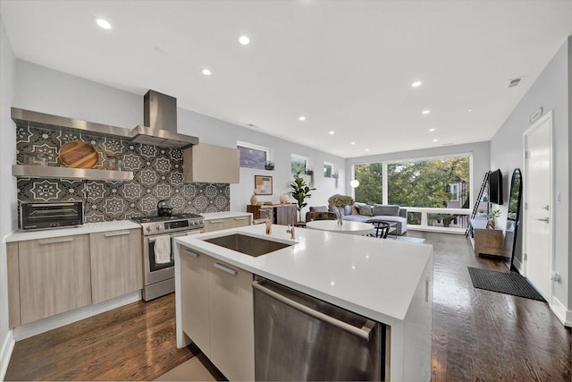 kitchen with modern cabinets, stainless steel appliances, light countertops, wall chimney range hood, and a sink