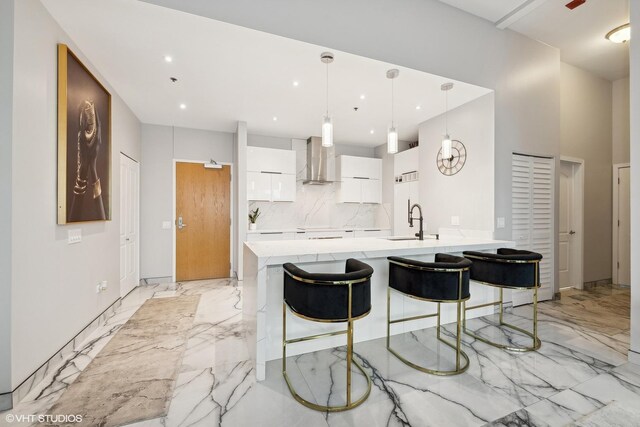 kitchen featuring pendant lighting, white cabinetry, sink, kitchen peninsula, and wall chimney exhaust hood