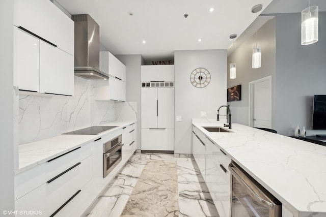 kitchen with pendant lighting, sink, light stone counters, stainless steel appliances, and wall chimney exhaust hood