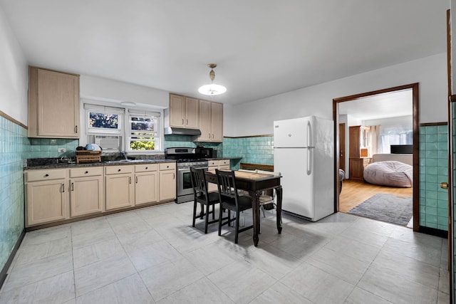 kitchen with white refrigerator, stainless steel range with gas cooktop, light brown cabinetry, and tile walls