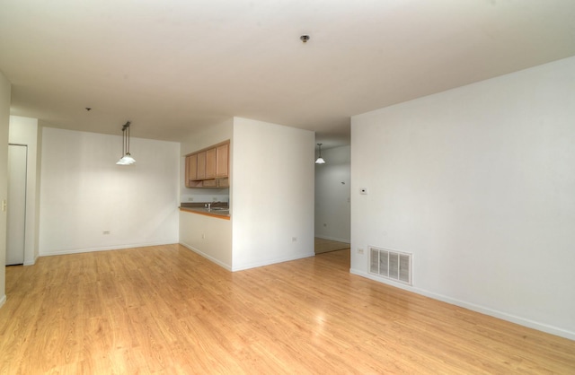 unfurnished living room featuring light wood-style floors, visible vents, a sink, and baseboards