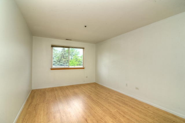 spare room featuring light wood-type flooring, visible vents, and baseboards