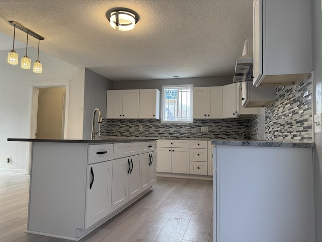 kitchen with a center island with sink, light hardwood / wood-style floors, pendant lighting, and white cabinets