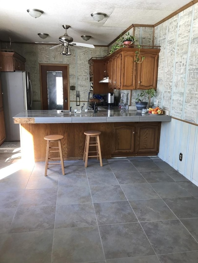 kitchen featuring crown molding, a breakfast bar area, stainless steel fridge, and kitchen peninsula