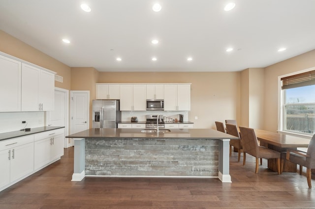 kitchen with dark wood finished floors, stainless steel appliances, dark countertops, a kitchen island with sink, and a sink