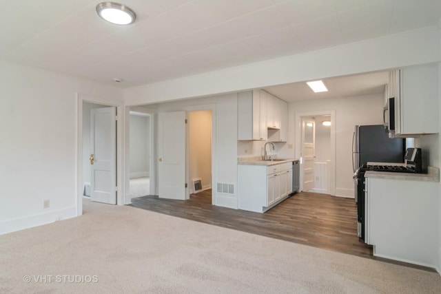 kitchen with stainless steel appliances, white cabinetry, sink, and dark carpet