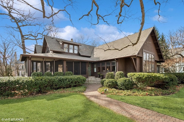 view of front of house featuring roof with shingles, a chimney, a front lawn, and a sunroom