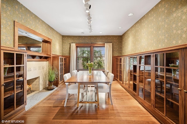 dining space with light wood-style flooring, track lighting, and wallpapered walls