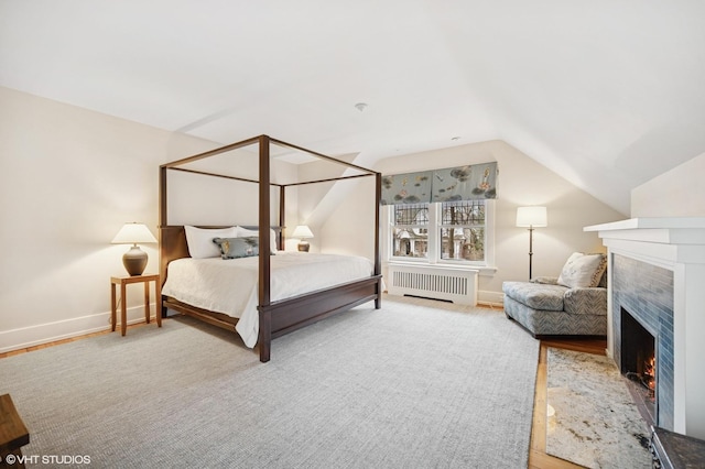 carpeted bedroom with a tiled fireplace, radiator, baseboards, and vaulted ceiling