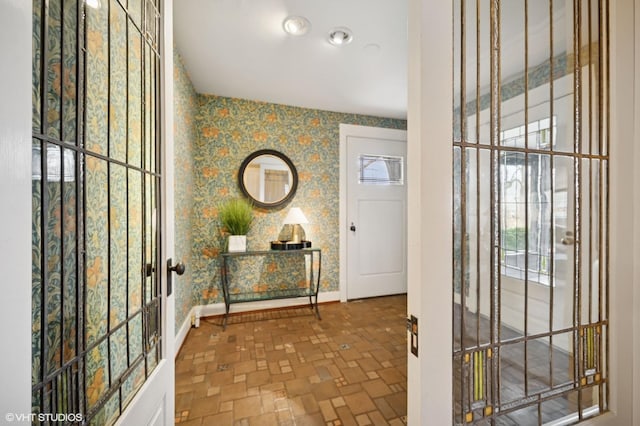 entrance foyer with wallpapered walls, brick floor, and baseboards