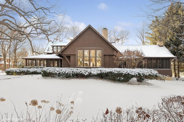 snow covered property with a chimney and a sunroom